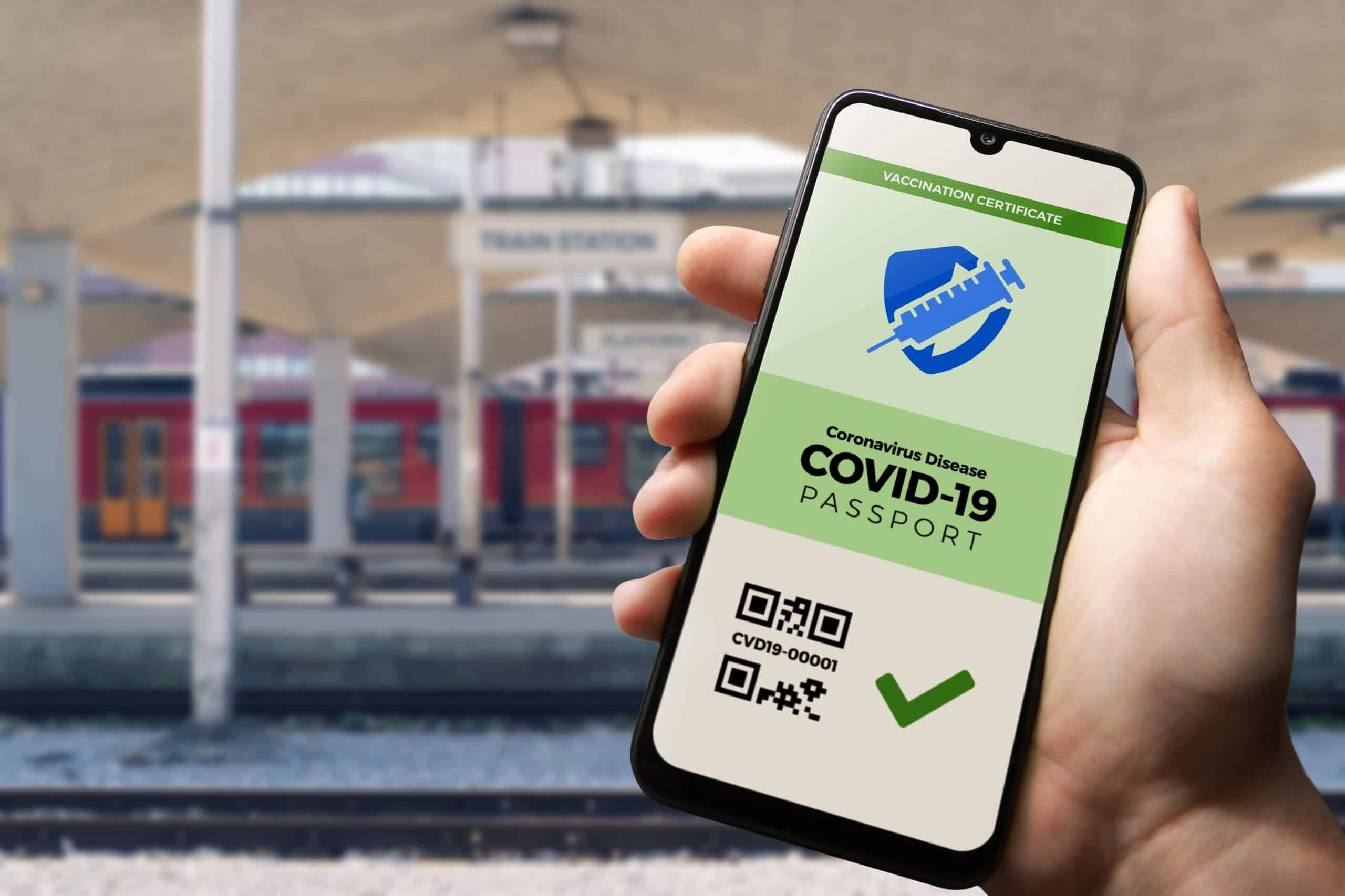 Hand hält Smartphone mit Grünem Pass vor Bahnsteig