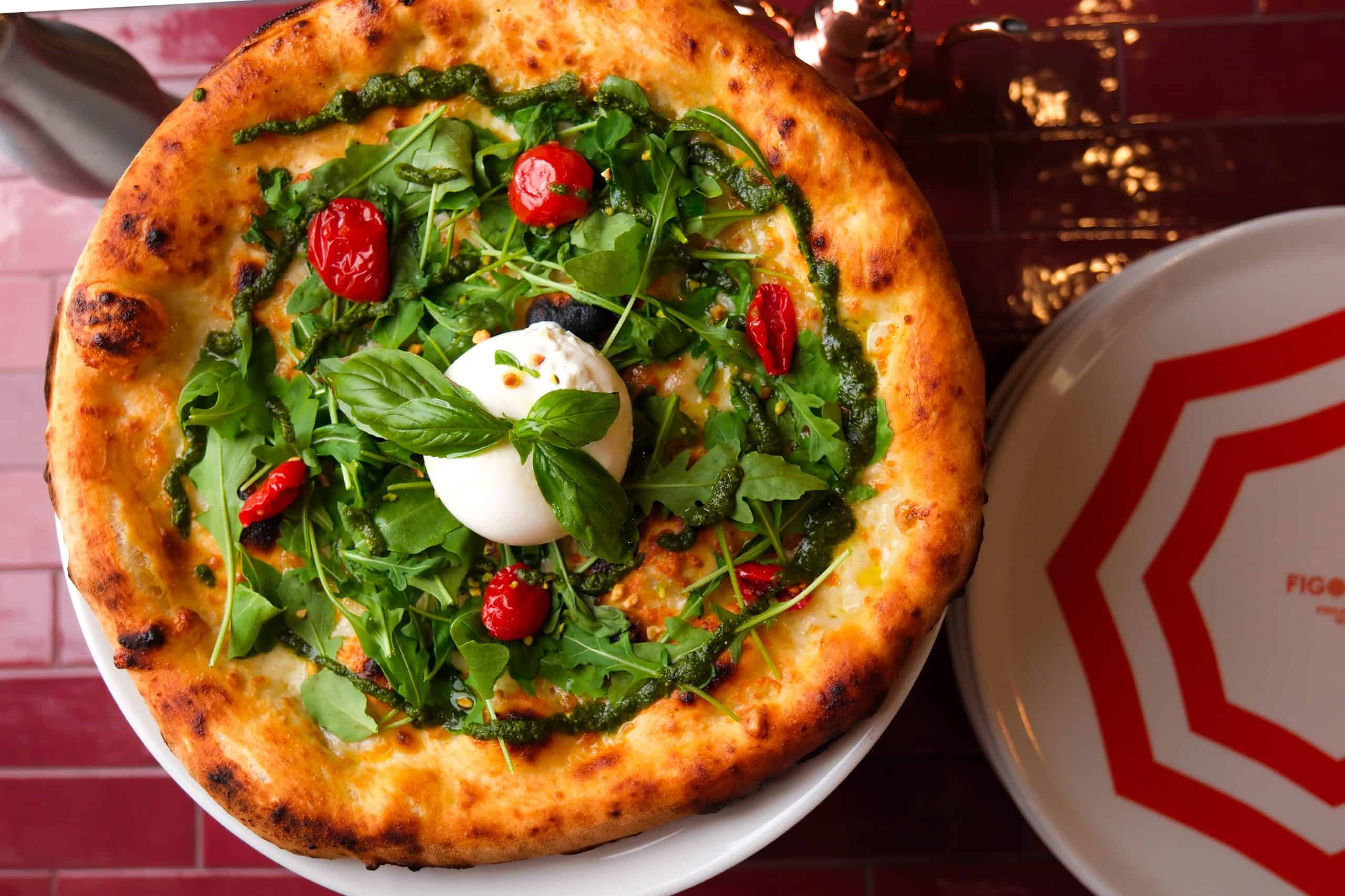 Goldbraun gebackener Pizzateig belegt mit frischem Rucola, Burrata und Tomaten