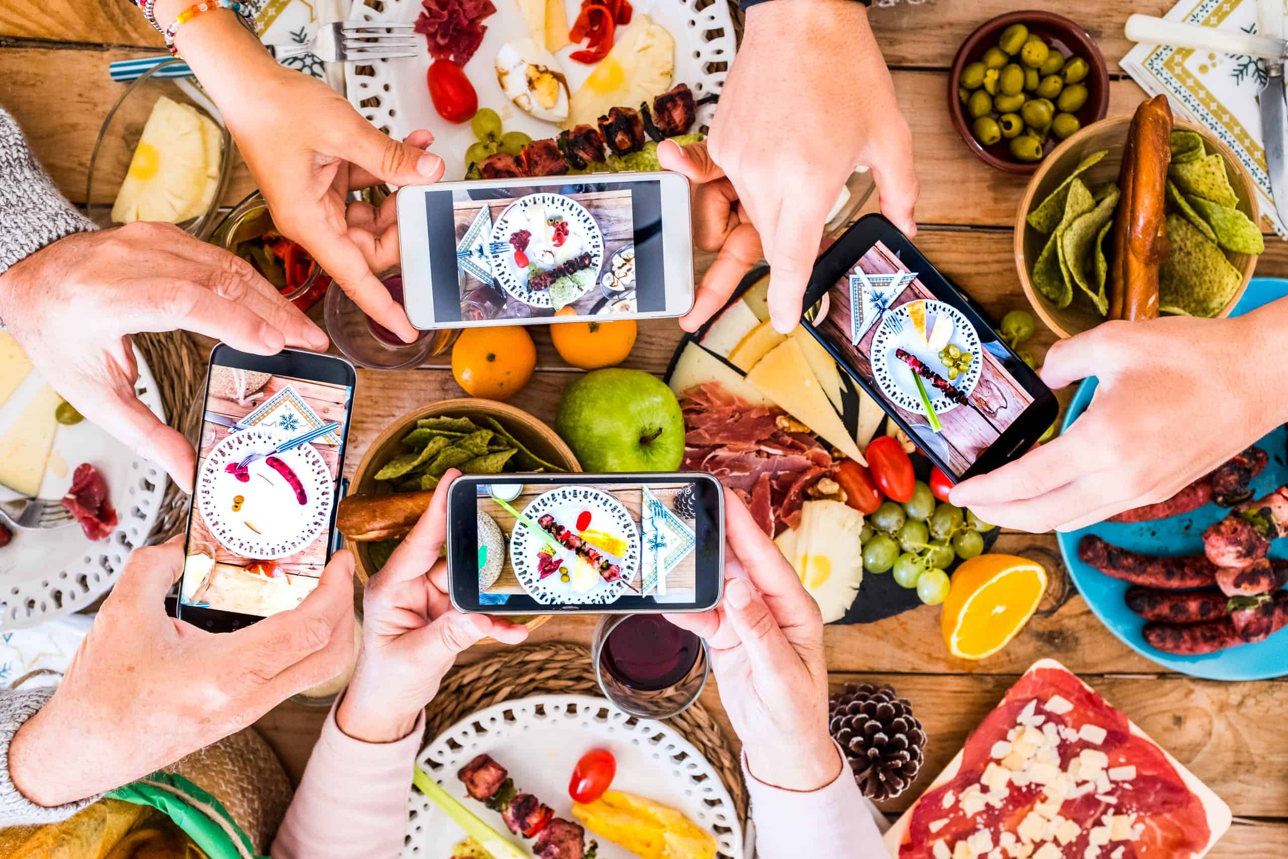 Food Influencer an einem Tisch, jeder lichtet mit seinem Handy das Essen ab